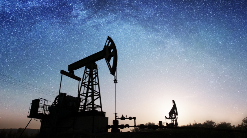 Siluet dua pompa minyak memompa minyak mentah di ladang minyak di bawah langit malam dengan bintang-bintang dan Bima Sakti.Peralatan industri minyak