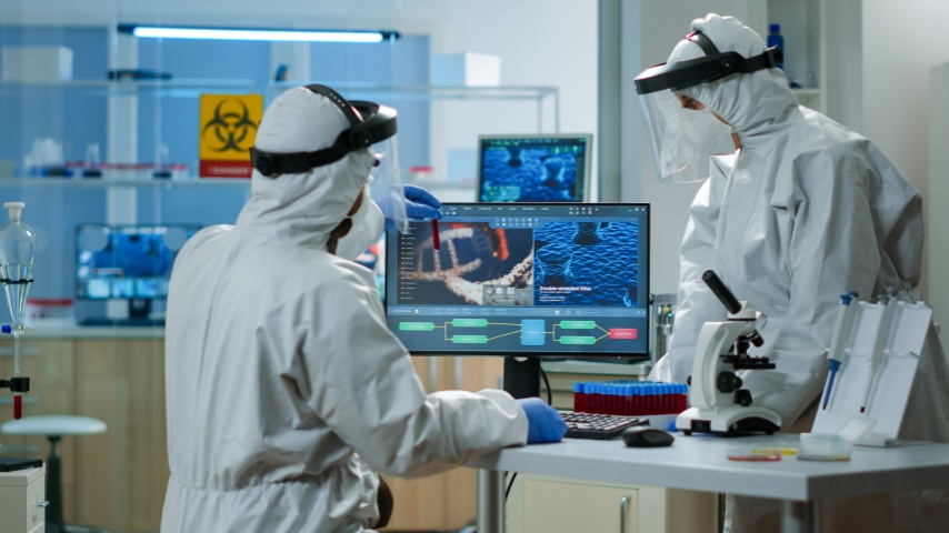 防護服を着た科学者が化学設備の整った実験室で血液サンプルの入った試験管を分析している。ハイテクと治療法を研究するテクノロジーを使用してワクチンの進化を調査する生物学者